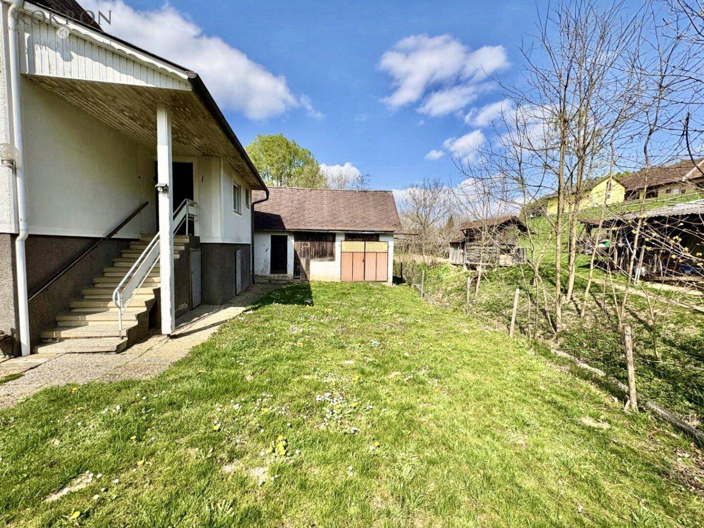 Seitenansicht des Hauses mit Außentreppe und einem Nebengebäude im grünen Gartenbereich.