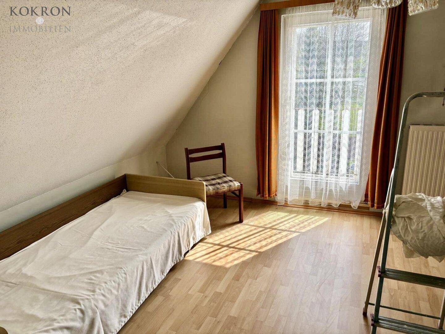 Helles Schlafzimmer mit Einzelbett, Laminatboden und Fenster mit Blick ins Grüne.