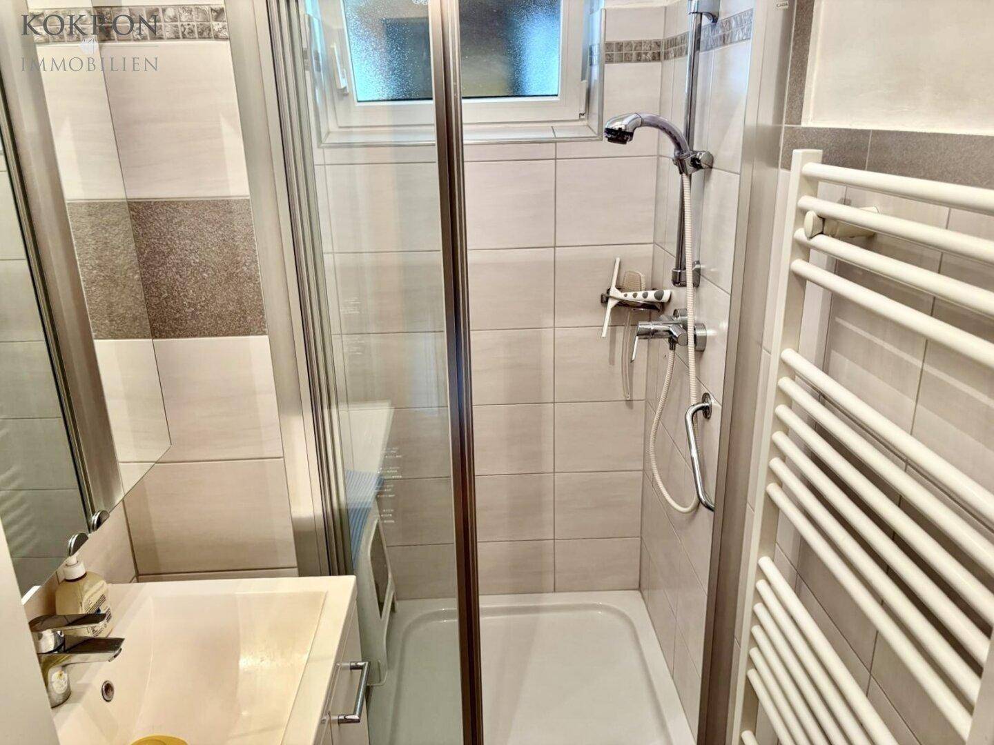 Modernisiertes Badezimmer mit Duschkabine, Waschbecken und beheiztem Handtuchhalter.