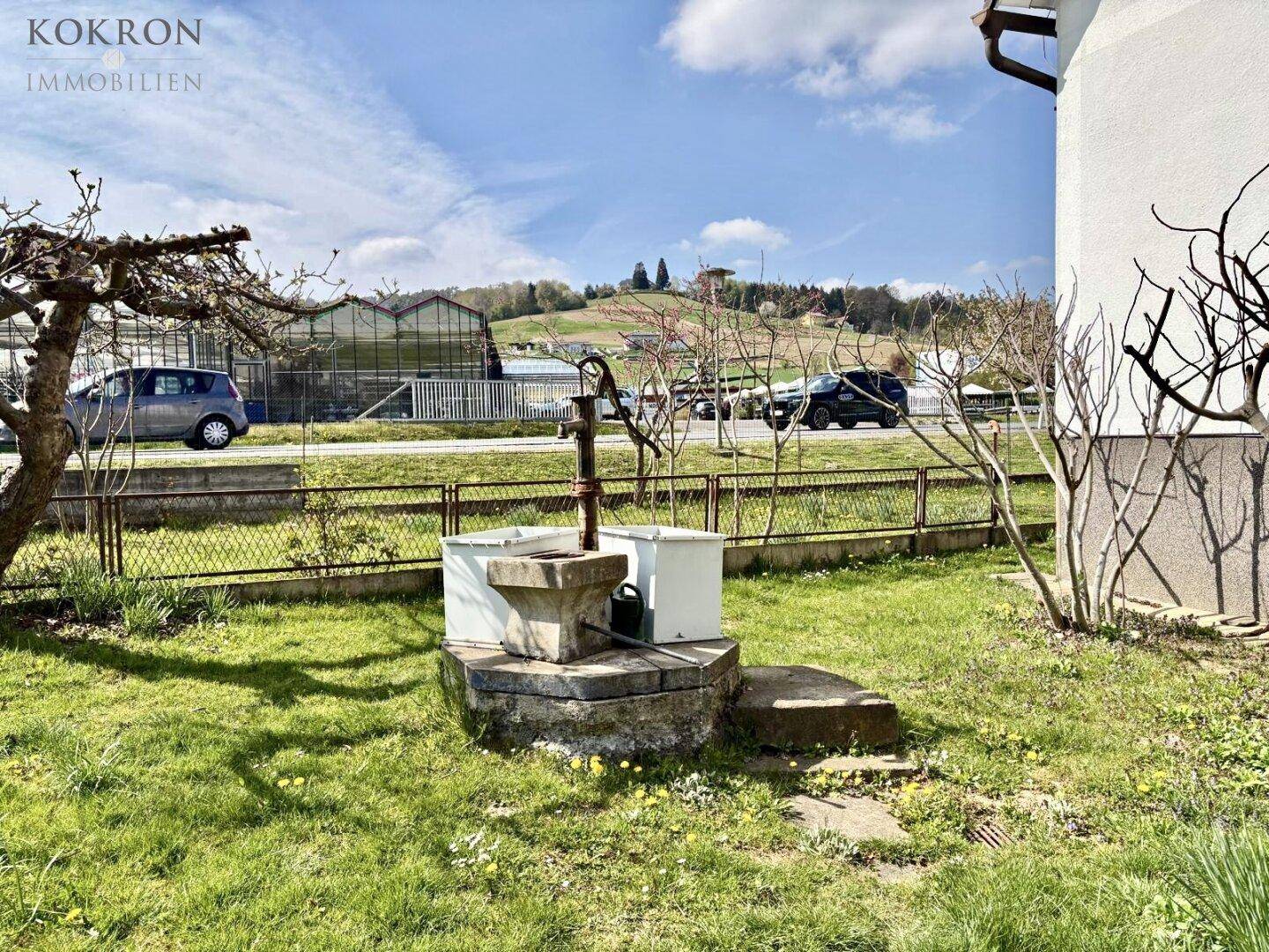 Grüner Gartenbereich mit einem alten Brunnen und Blick auf die umliegende Landschaft.