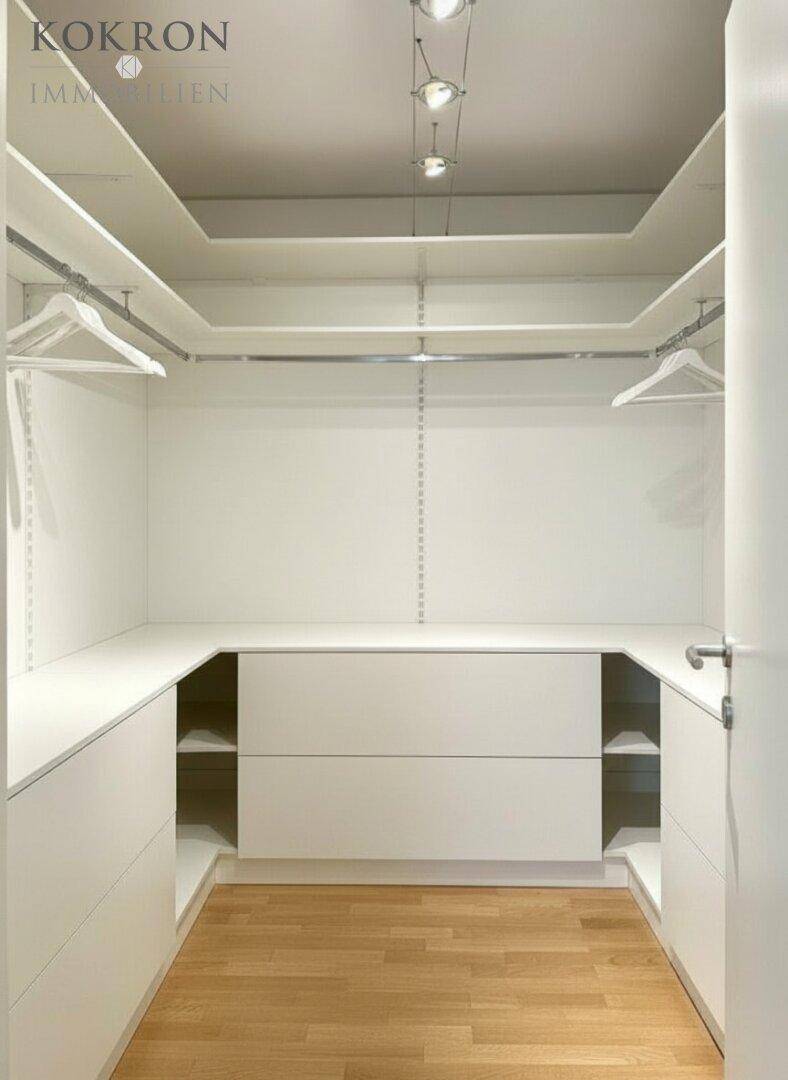 Geräumiger begehbarer Kleiderschrank mit viel Stauraum, integrierten Schubladen und heller Beleuchtung.