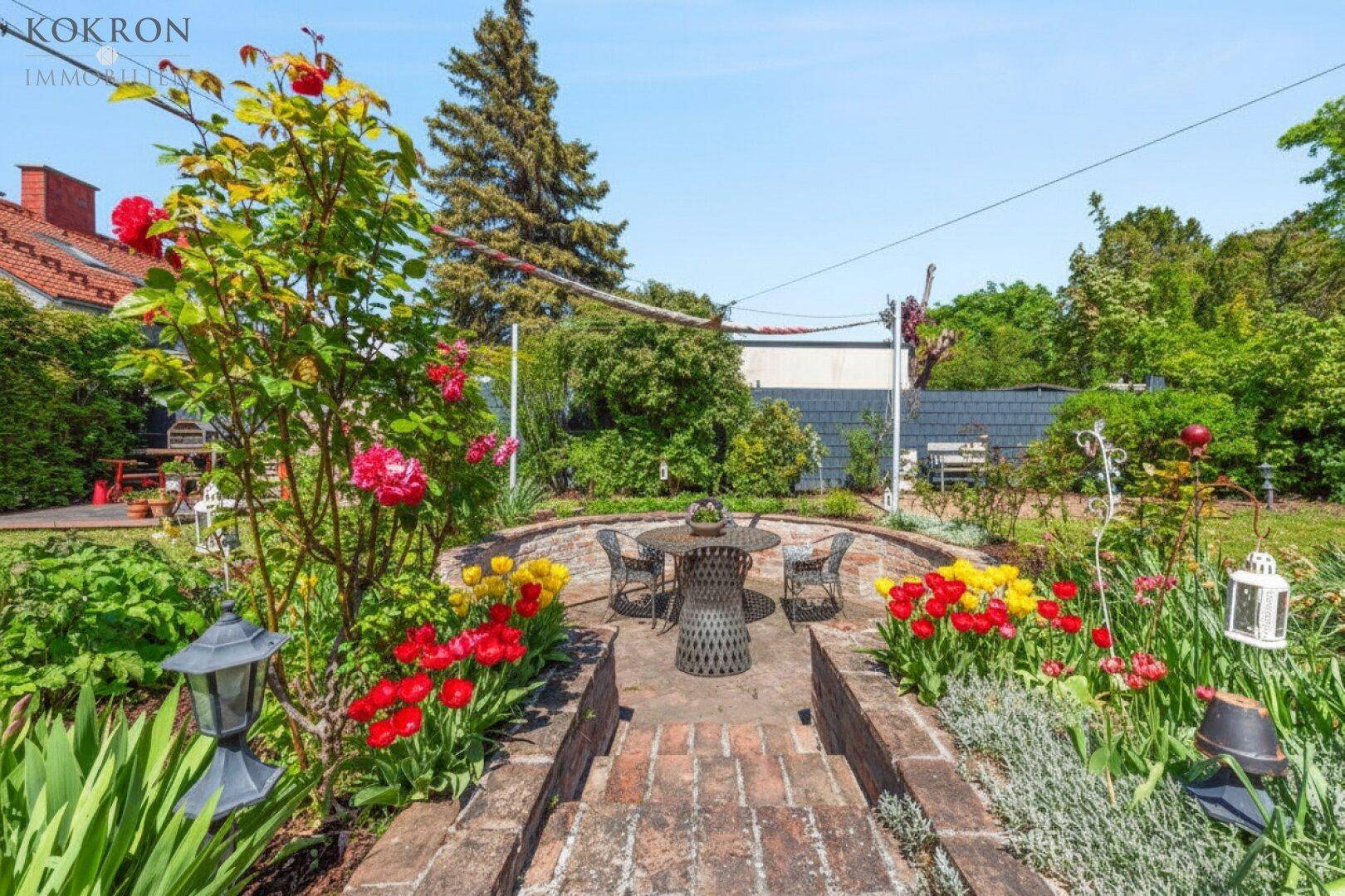 Gepflegter Garten mit gemauerter Sitzecke, bunten Blumenbeeten und üppigem Grün.
