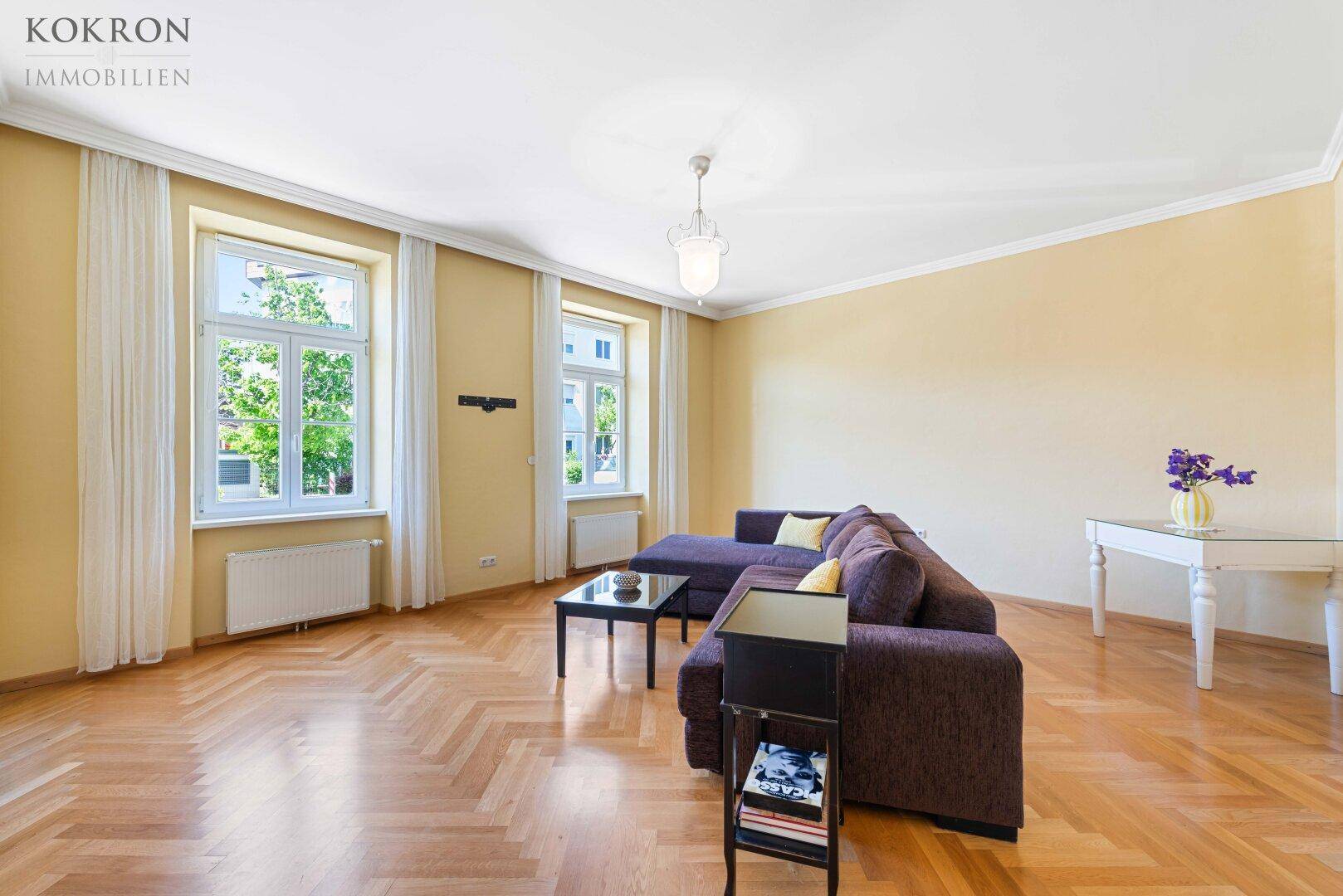 Helles Wohnzimmer mit Fischgrätparkett, großen Fenstern und einem gemütlichen Sofa.