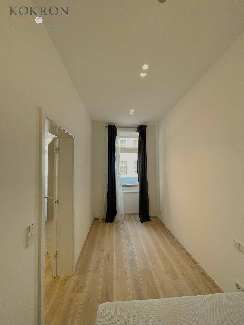 Schmaler Schlafbereich mit Holzboden, einem Fenster und dunklen Vorhängen.