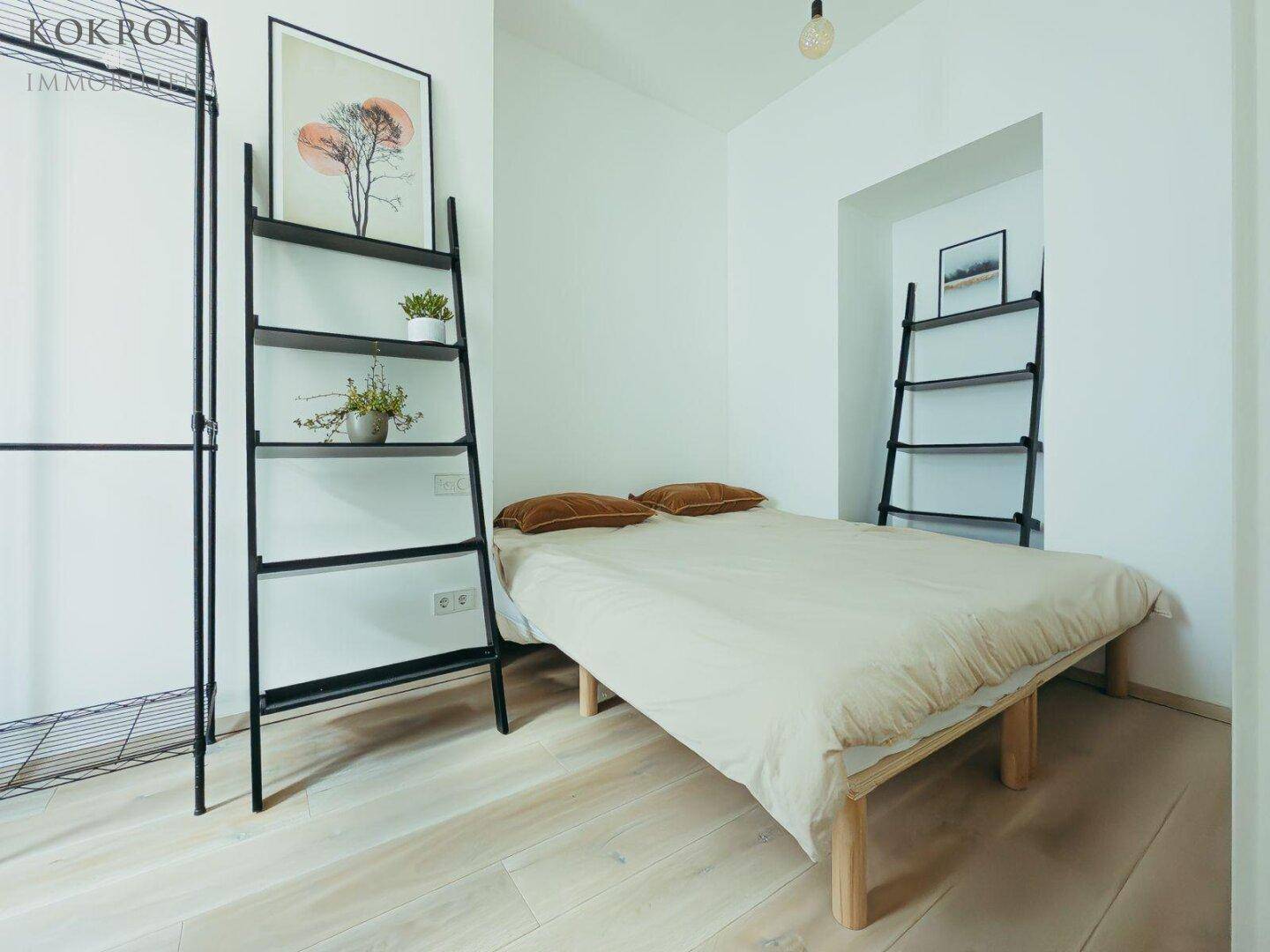 Schlafzimmer mit Holzboden, Bett und zwei modernen Regalen an den Wänden.