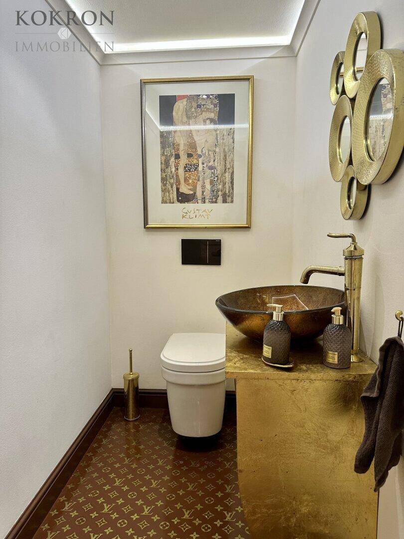 Exklusives Gäste-WC mit goldenen Armaturen, einzigartigem Waschbecken und auffälligem Bodenbelag.