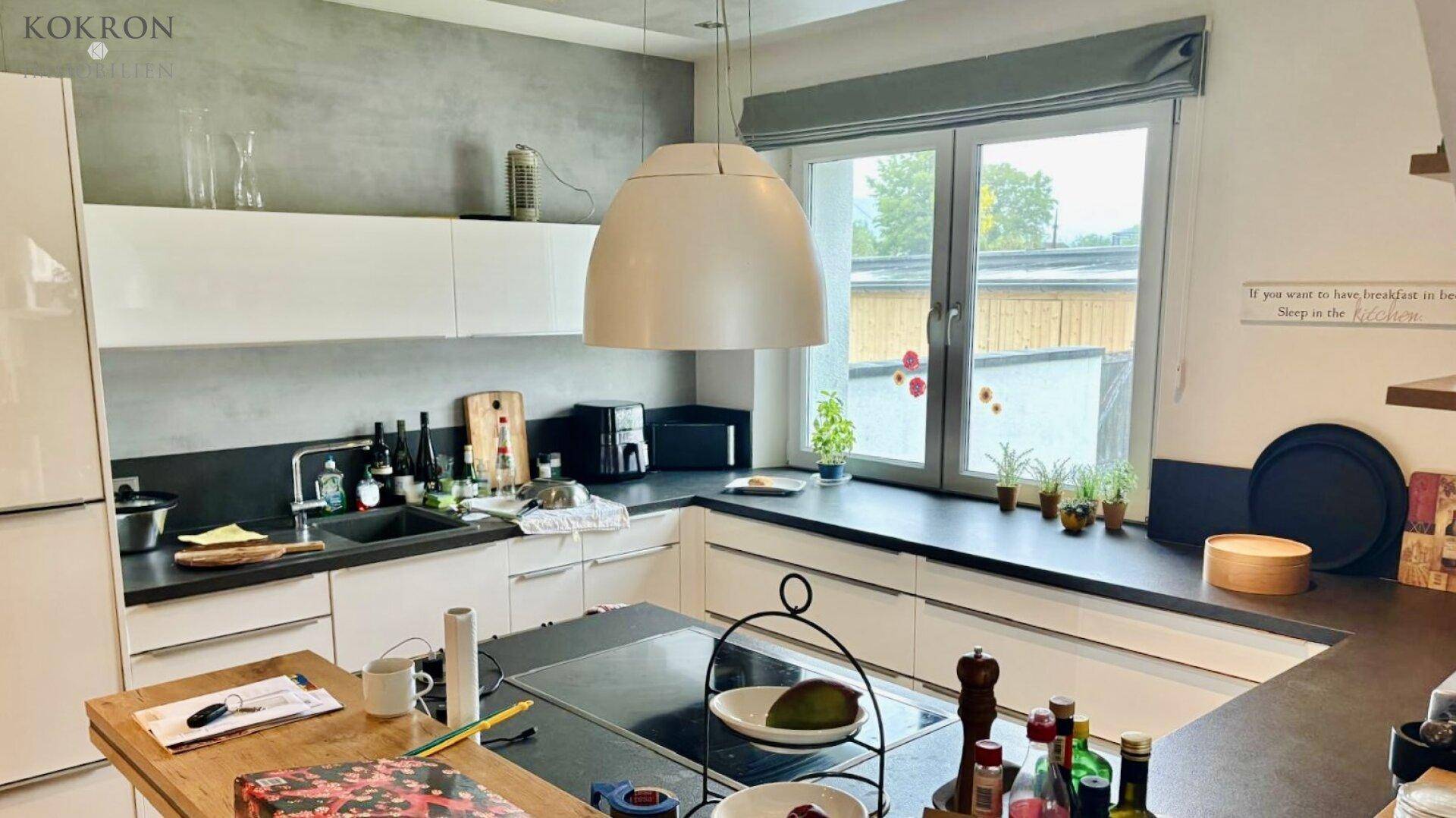 Moderne Küche mit weißen Schränken, dunklen Arbeitsplatten und großem Fenster über der Spüle.