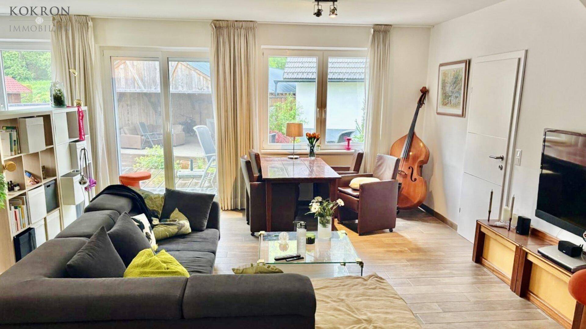 Gemütlicher Wohn-Essbereich mit großem Sofa, Holztisch und Zugang zu einem Außenbereich.