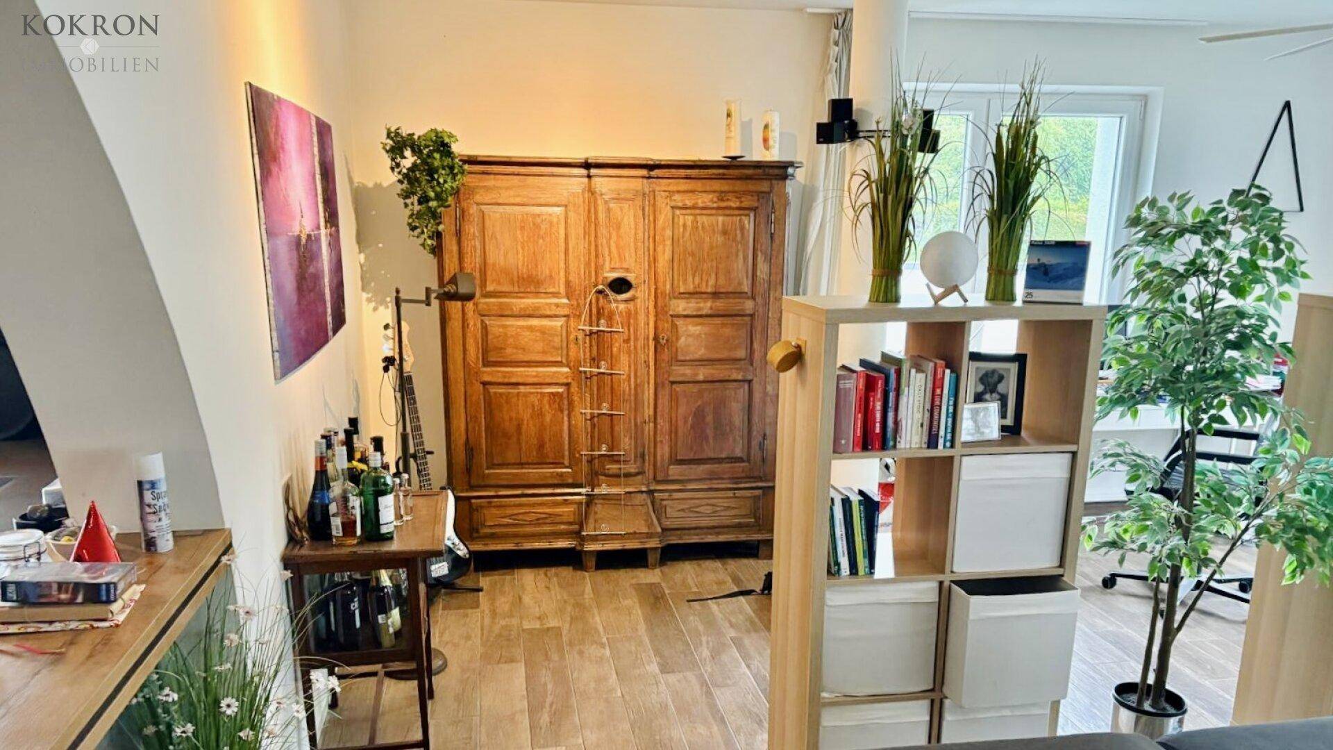 Heller Raum mit antikem Holzschrank, Bücherregal und Holzboden, mit Zugang nach draußen.
