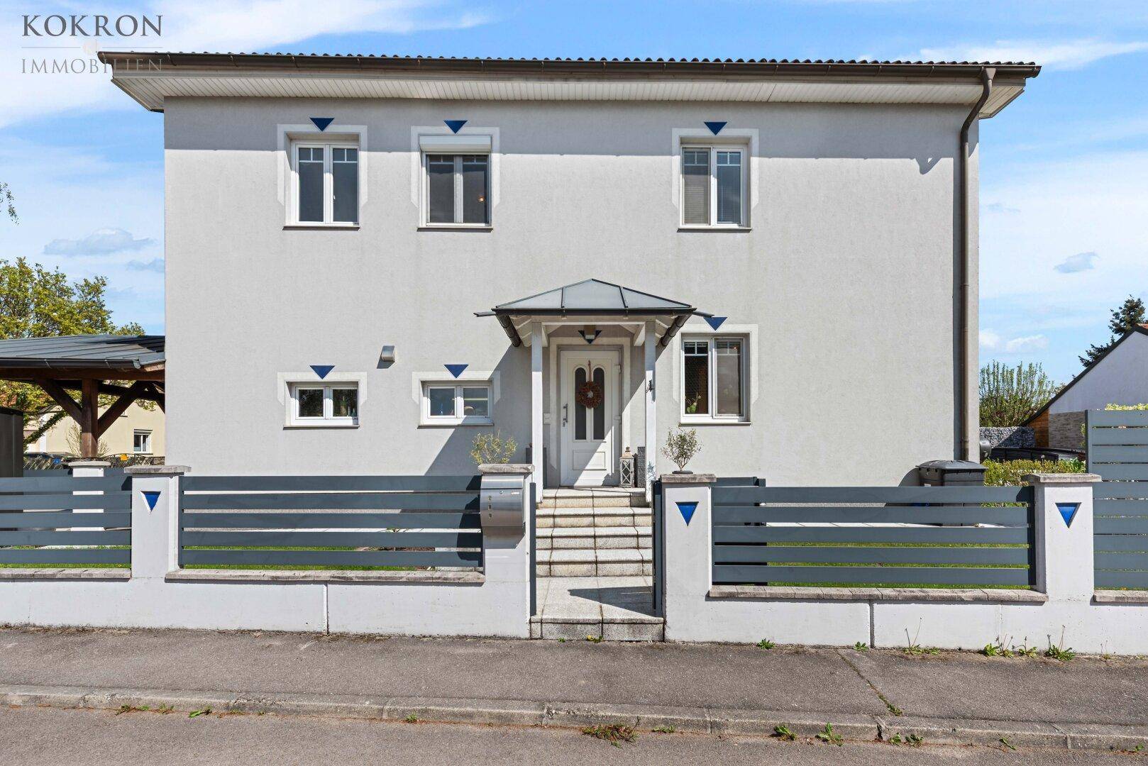 Modernes Einfamilienhaus mit heller Fassade, gepflegtem Vorgarten und einladendem Eingangsbereich.