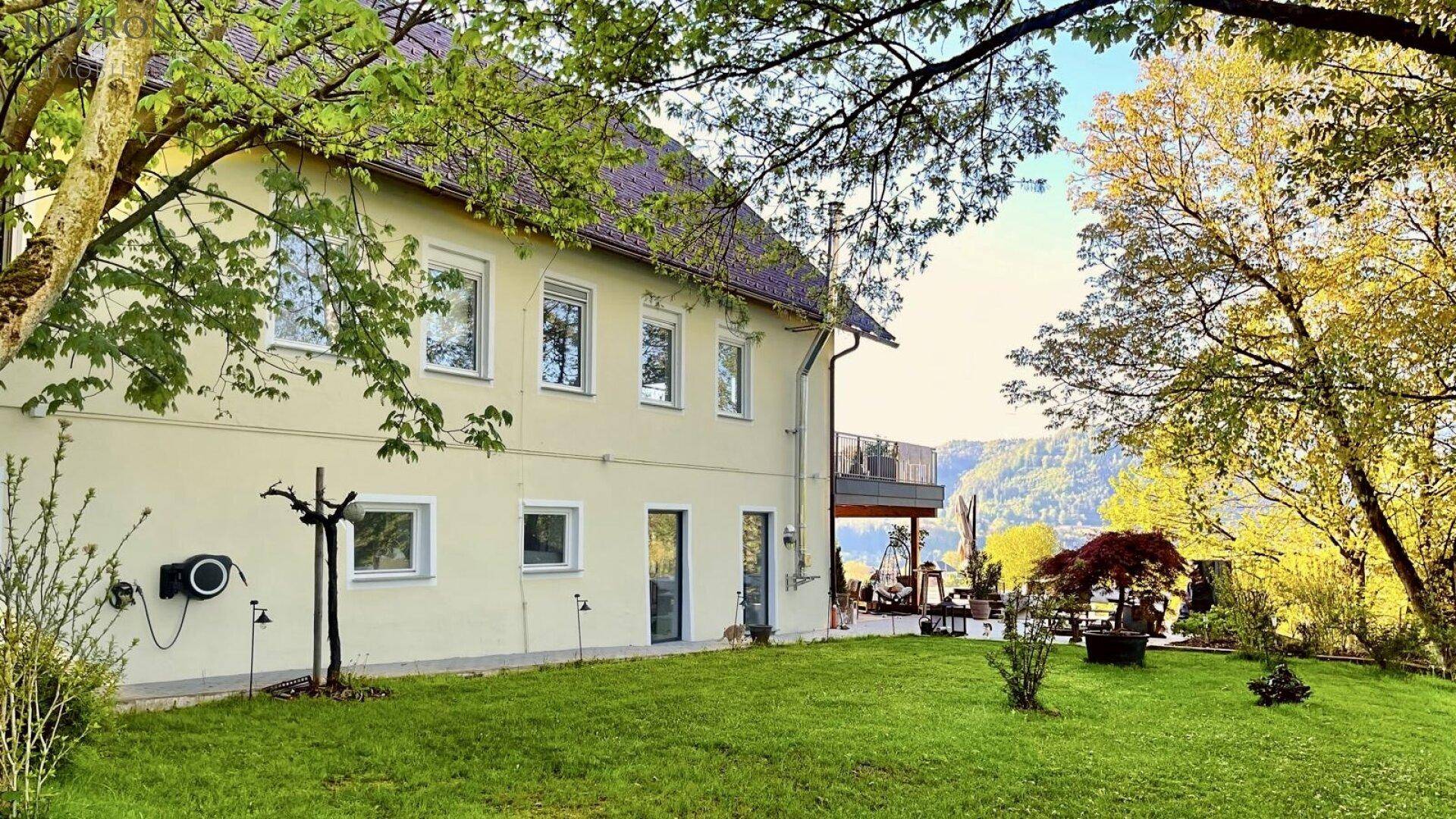 Seitenansicht des Hauses mit gepflegtem Rasen und einem Balkon mit Blick auf die umliegende Landschaft.