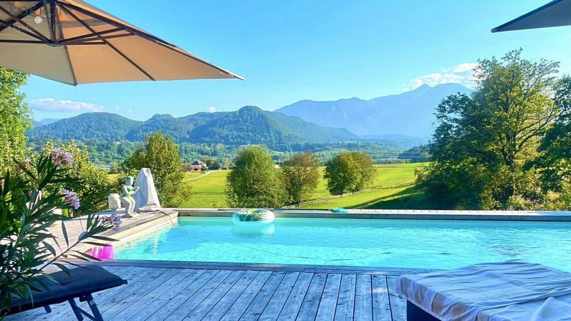 Außenpool mit Holzdeck und Sonnenschirm, der einen atemberaubenden Blick auf die umliegende Berglandschaft bietet.