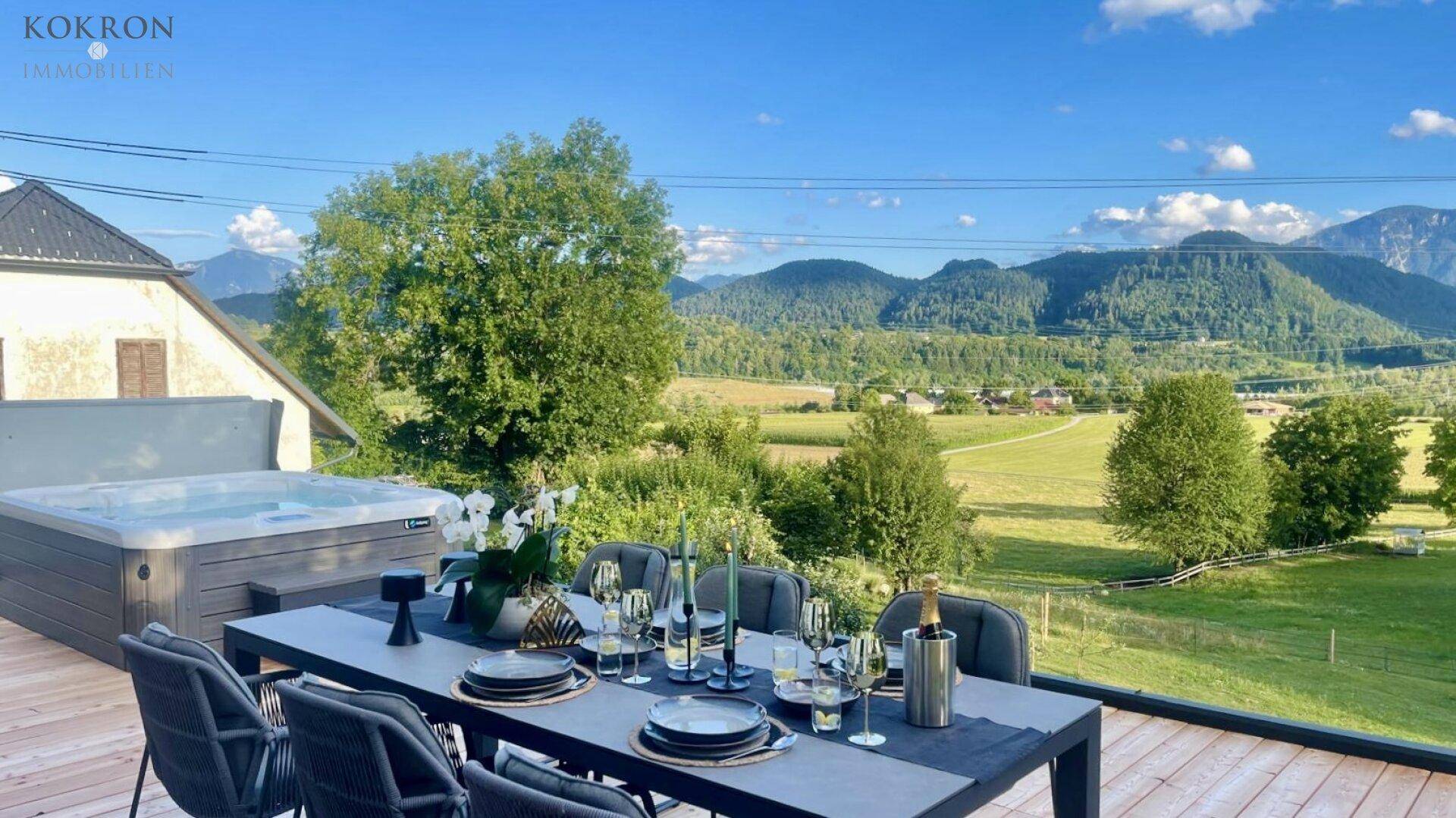 Gemütlicher Essbereich im Freien auf einer Holzterrasse mit Whirlpool und Panoramablick auf die Berge.