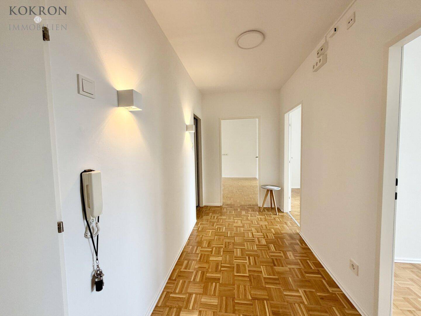 Heller Flur mit Parkettboden und modernen Wandleuchten, führt zu weiteren Räumen.