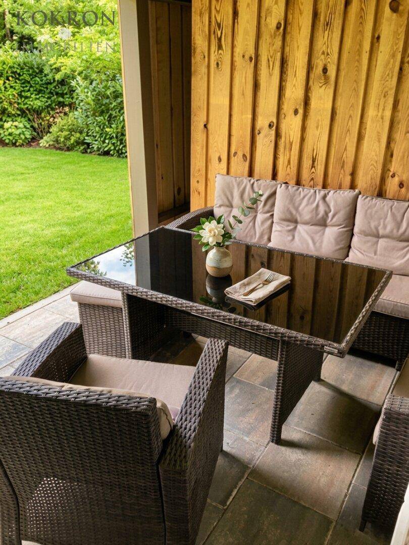 Gemütliche Terrasse mit Rattanmöbeln und Glastisch, umgeben von Holzverkleidung und Grün.