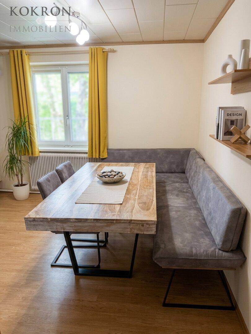 Gemütlicher Essbereich mit Holztisch, gepolsterter Sitzbank und gelben Vorhängen am Fenster.