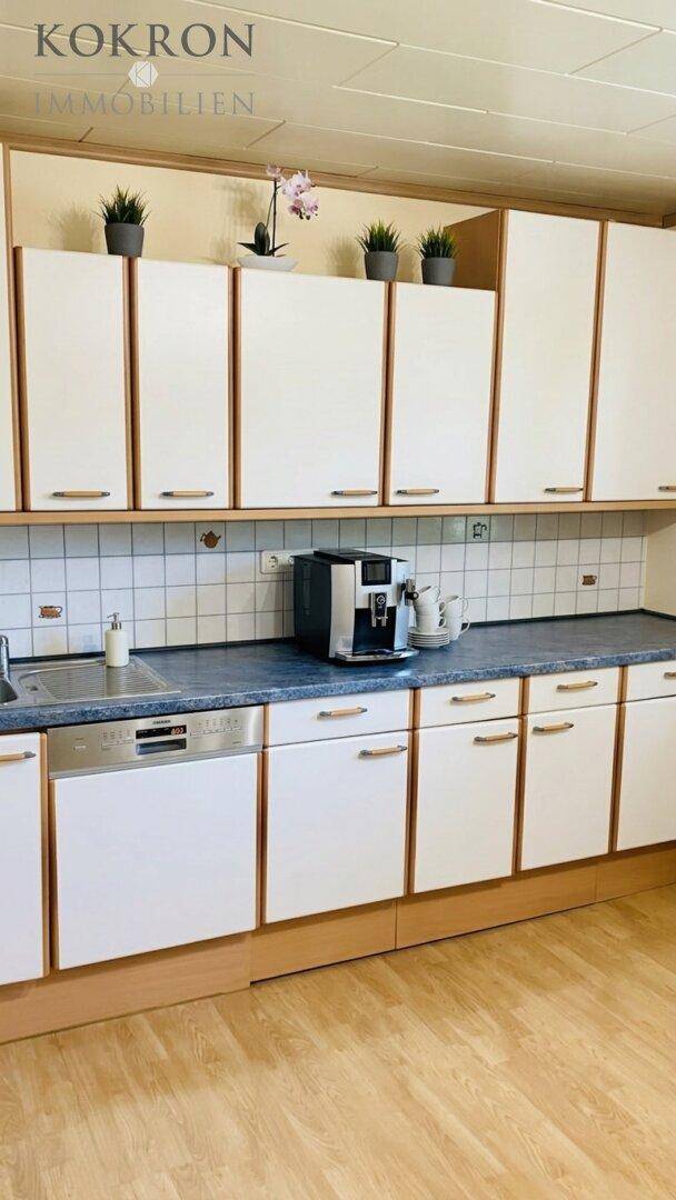 Funktionale Küche mit weißen Schränken, integriertem Geschirrspüler und Kaffeemaschine.