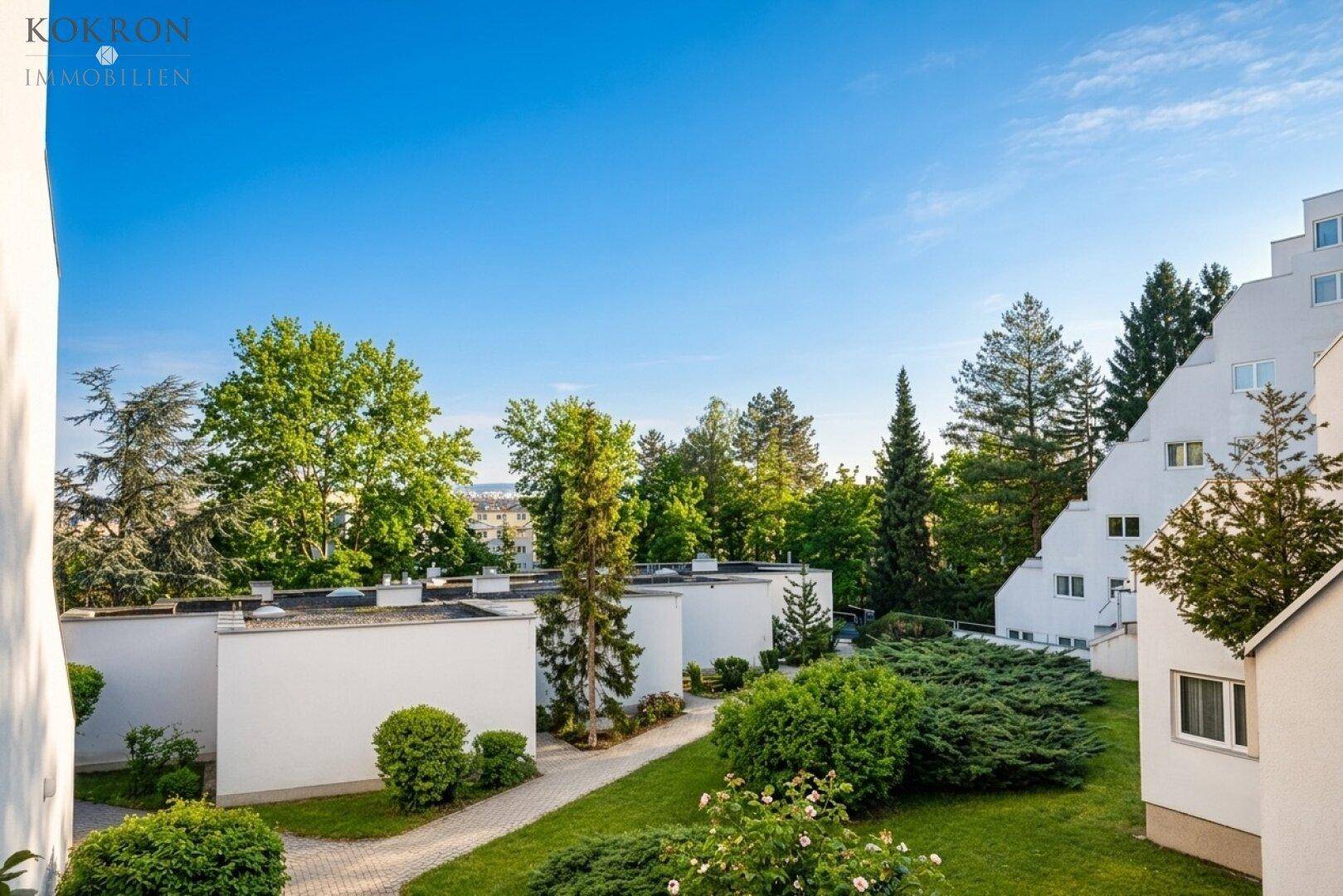 Außenansicht der Wohnanlage mit gepflegten Grünflächen und Bäumen unter blauem Himmel.