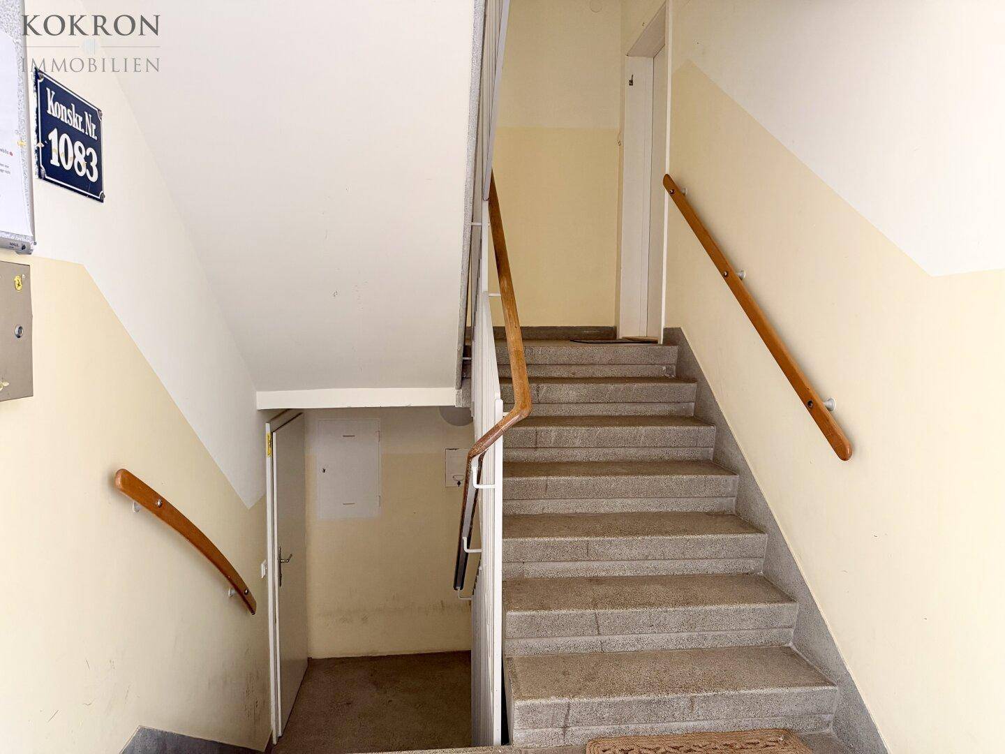 Treppenhaus mit Steinstufen, hellen Wänden und Holzhandläufen in einem Mehrfamilienhaus.