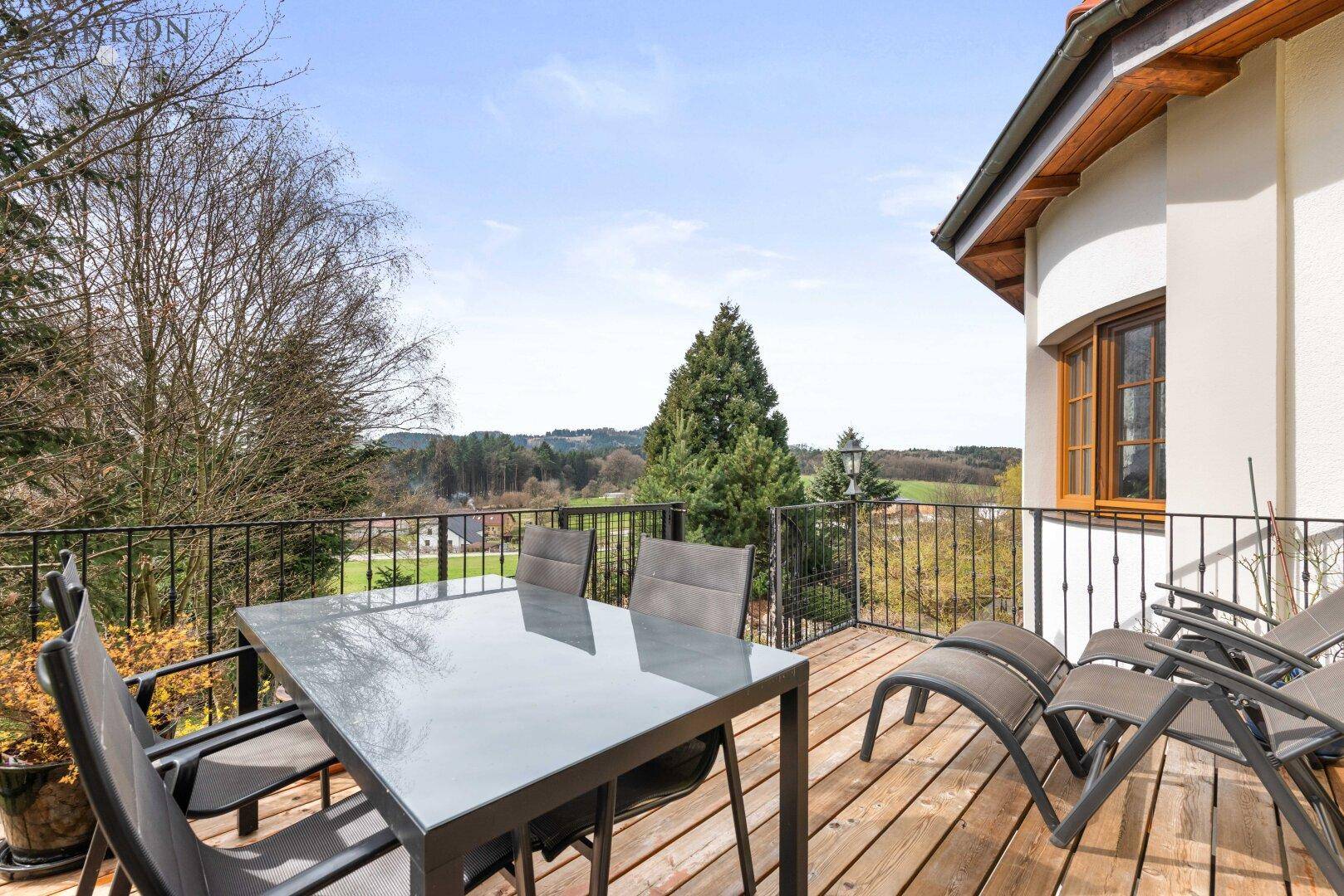 Geräumiger Balkon mit Holzboden, Gartenmöbeln und weitem Blick über die grüne Landschaft.