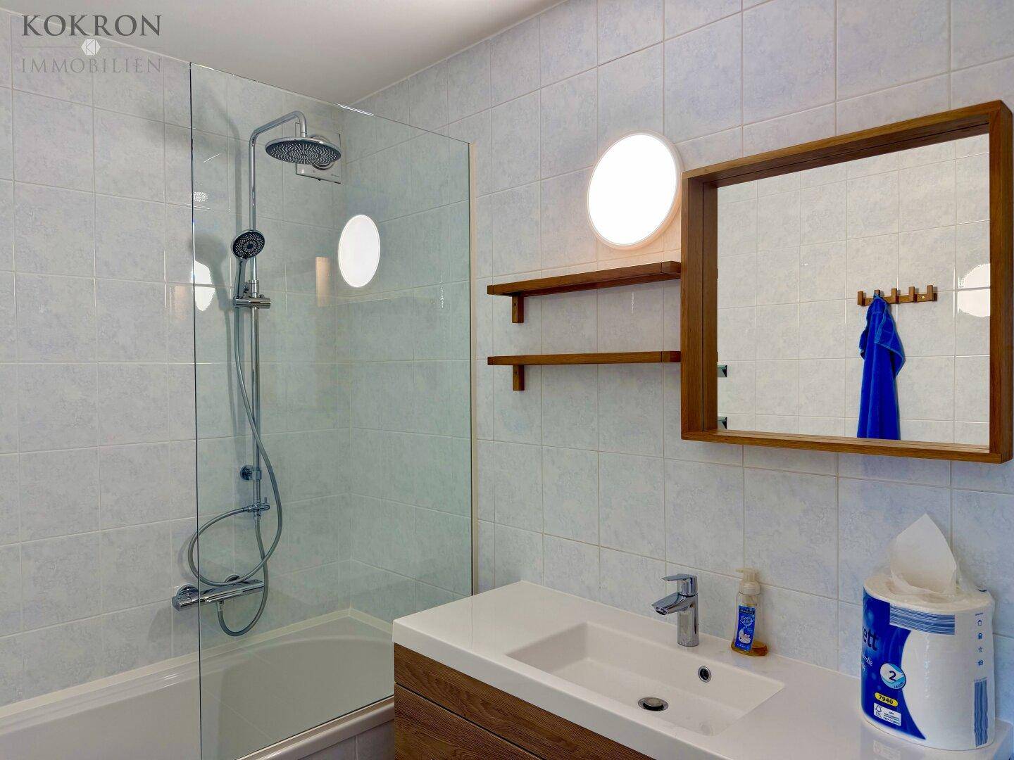 Modernes Badezimmer mit Dusch-Badewannen-Kombination, Einzelwaschbecken und Holzspiegel.