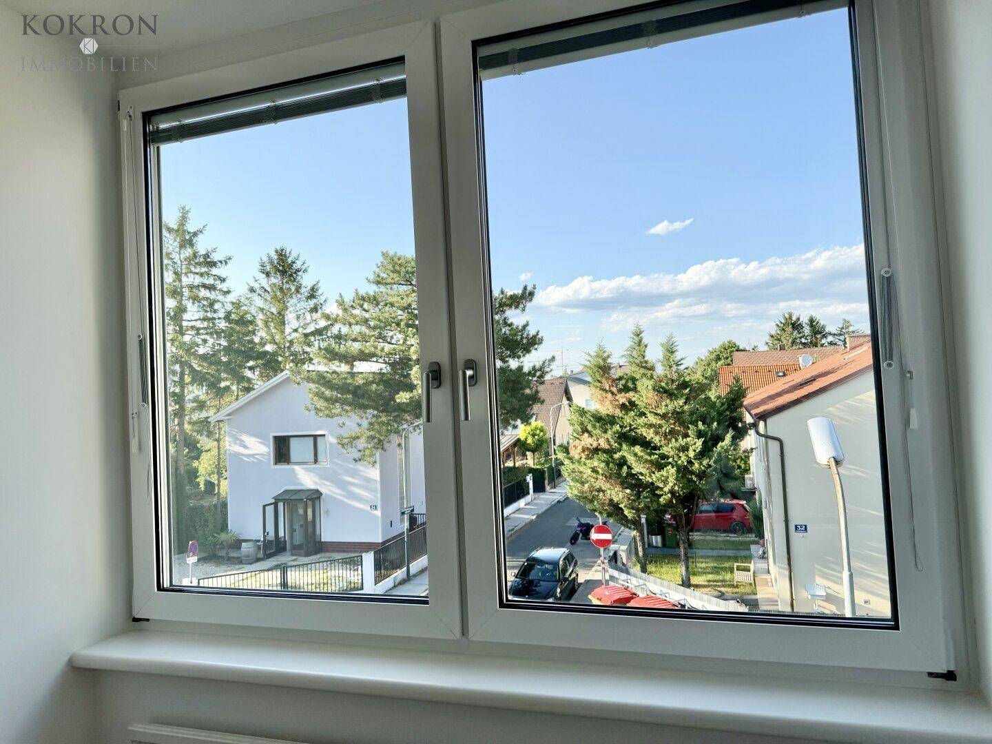 Blick aus dem Fenster auf eine ruhige Wohnstraße mit Häusern und viel Grün.