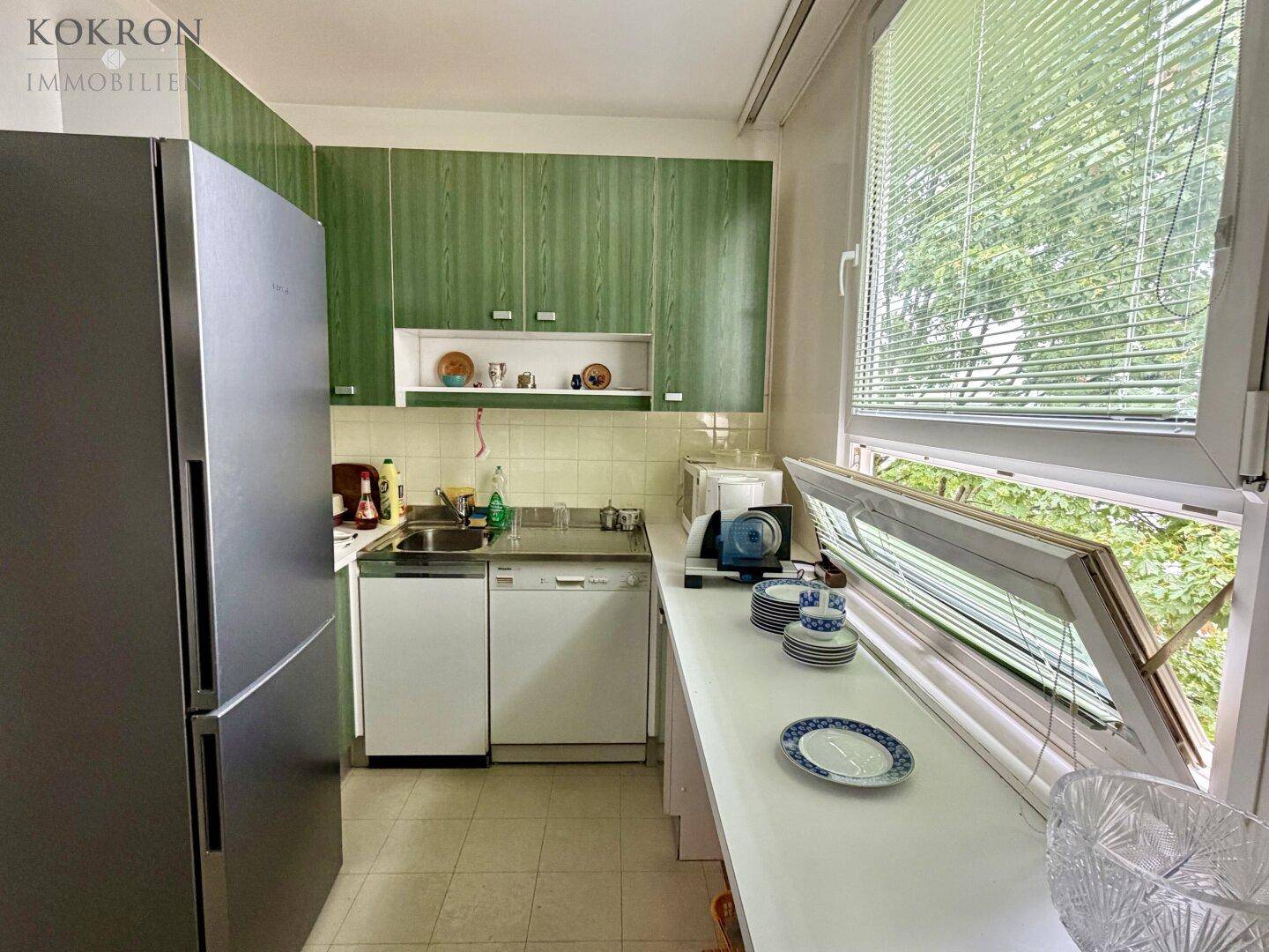 Küche mit grünen Holzschränken, integriertem Geschirrspüler und Kühlschrank, mit Fenster.