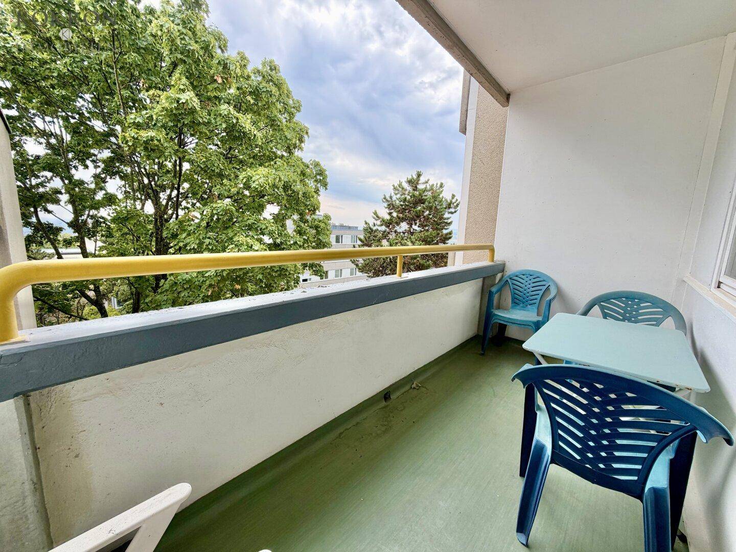 Balkon mit einfacher Kunststoffbestuhlung und Blick ins Grüne, umgeben von Bäumen.