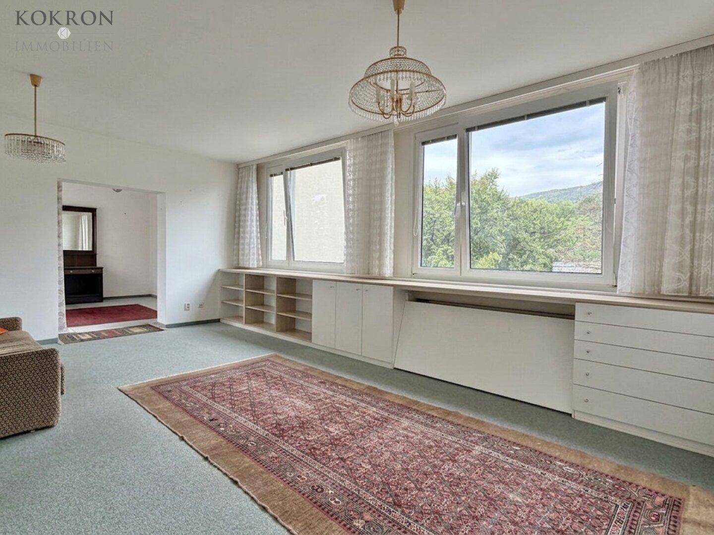 Geräumiges Wohnzimmer mit Teppichboden, großen Fenstern und eingebauten Schränken, Blick ins Grüne.