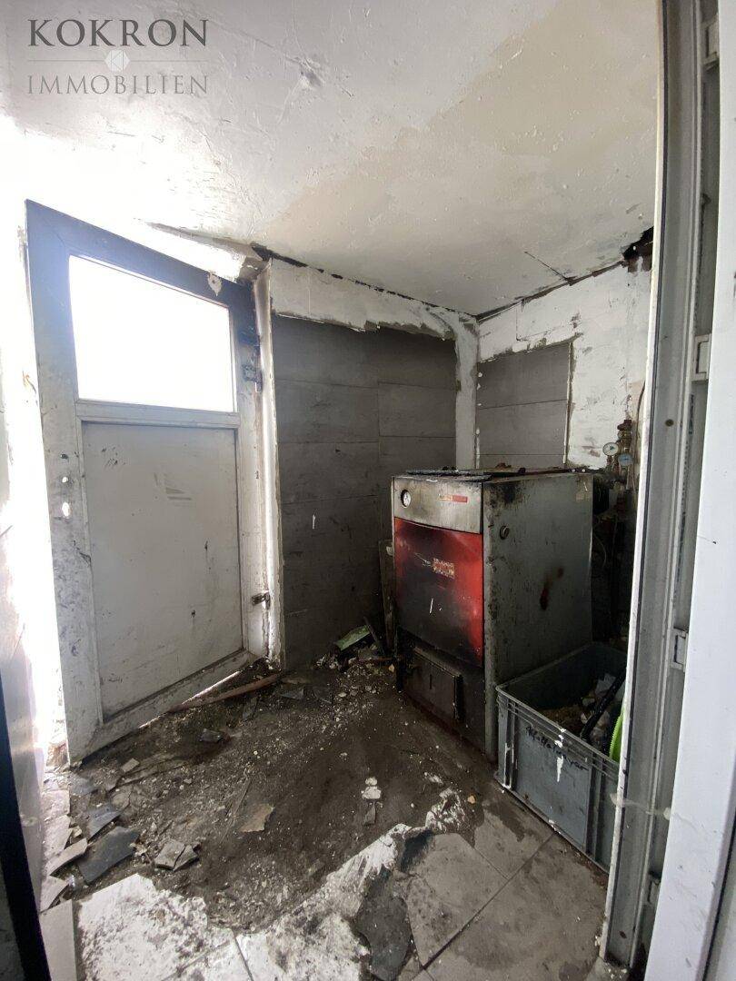 Verwahrloster Heizungsraum mit altem Boiler und Schmutz auf dem Boden, dringend sanierungsbedürftig.