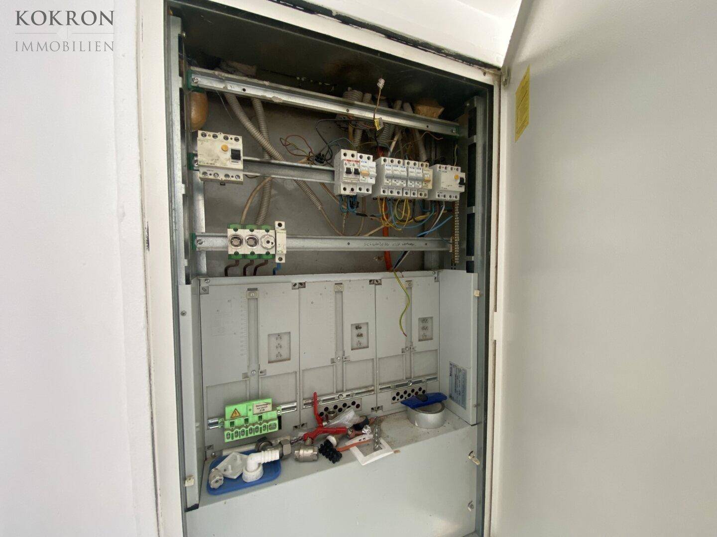 Offener Sicherungskasten mit elektrischen Leitungen und Schaltern, Teil der technischen Gebäudeausstattung.