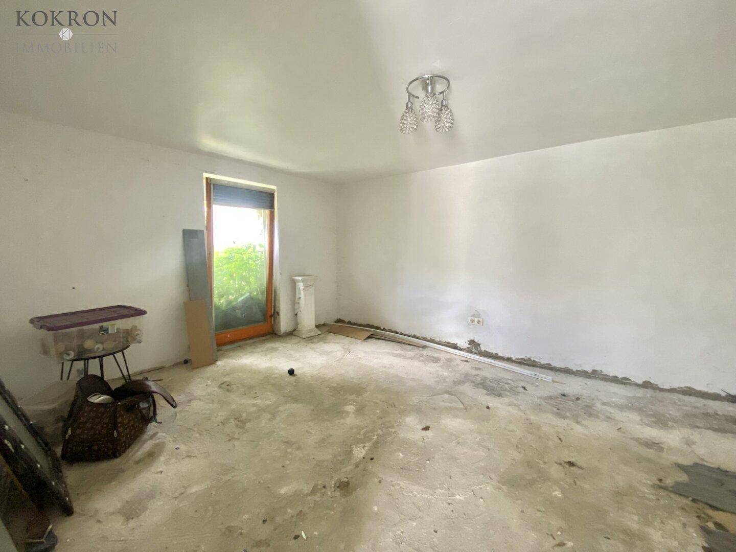 Leerer Raum mit Betonboden und einem Fenster, in sanierungsbedürftigem Zustand mit natürlichem Lichteinfall.
