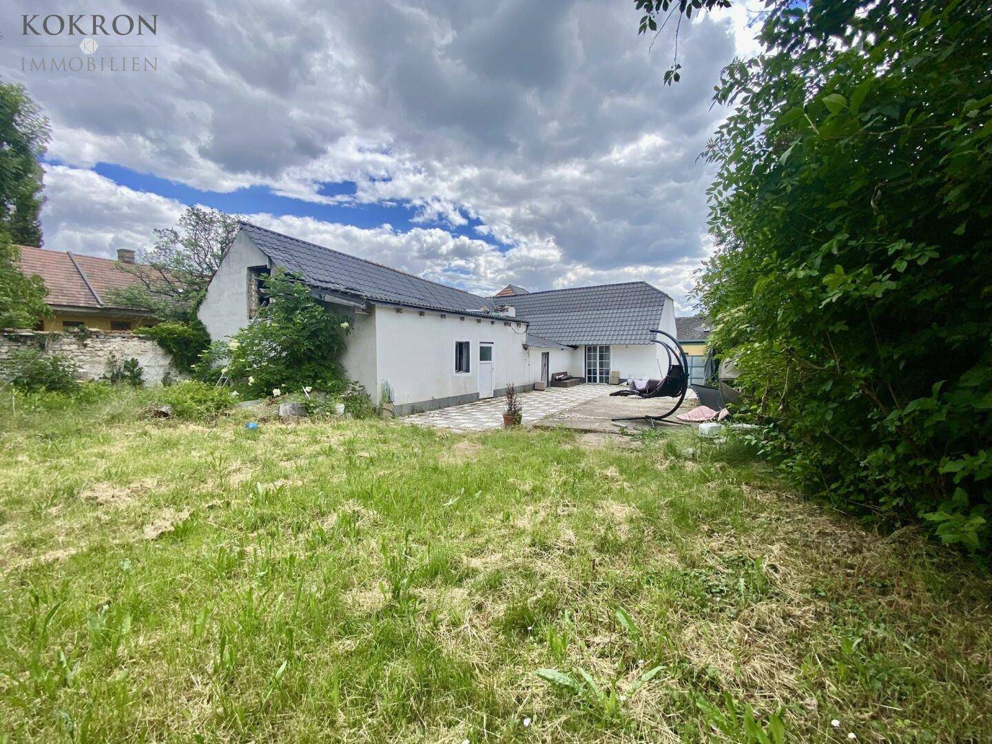 Rückseite des Hauses mit Gartenfläche, Rasen und kleiner Terrasse unter bewölktem Himmel.