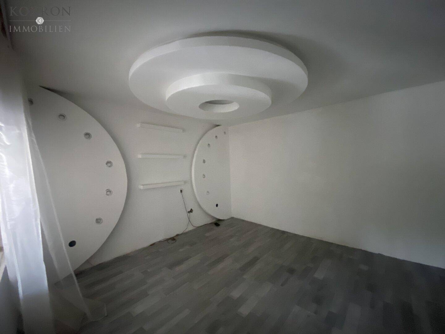 Leerer Raum mit dekorativer Deckenbeleuchtung und modernem grauen Laminatboden, bereit zur Einrichtung.