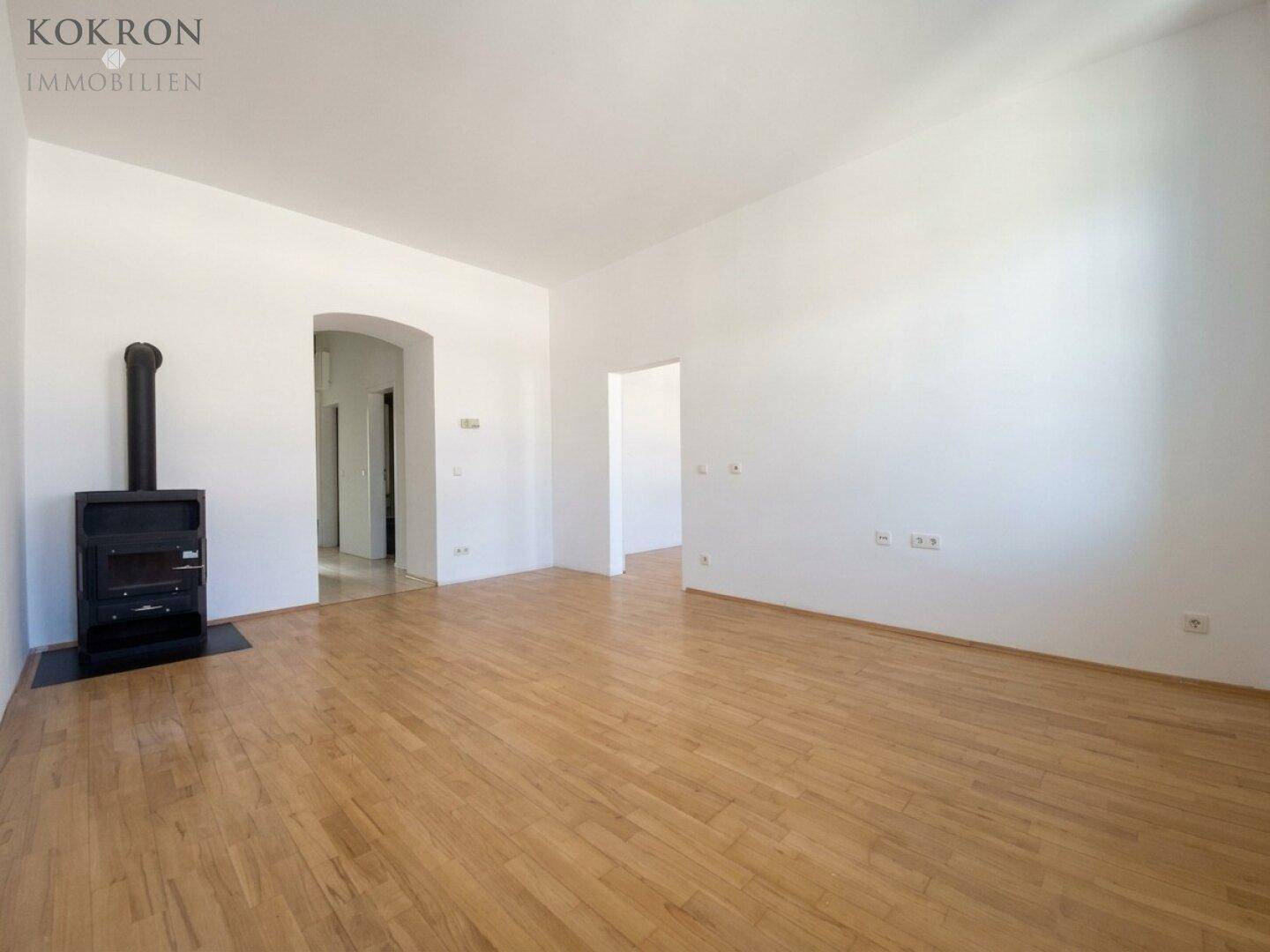 Geräumiges Wohnzimmer mit Holzboden und Zugang zu weiteren Räumen durch einen eleganten Bogen.