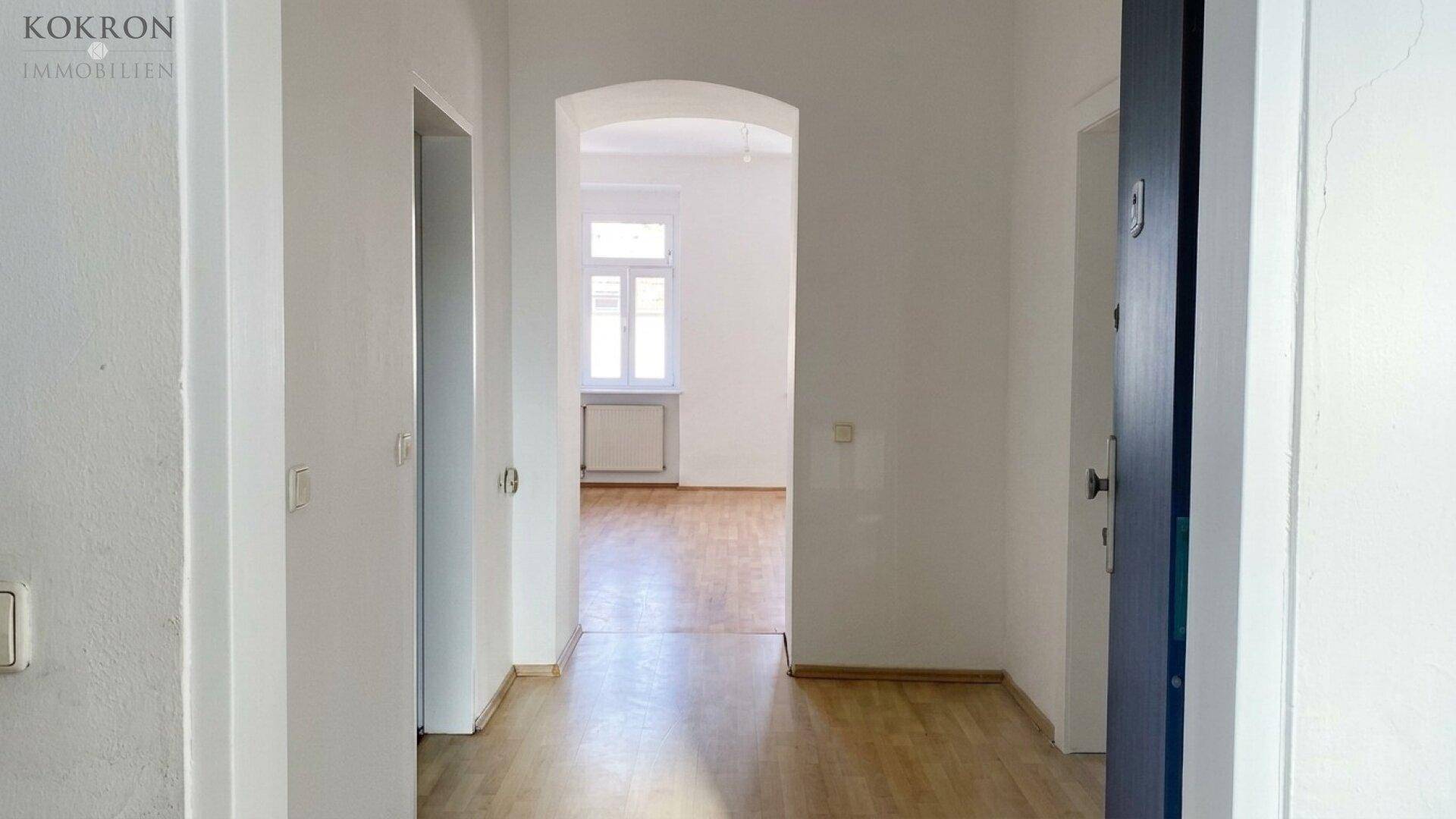 Heller Flur mit Holzboden, weiß gestrichenen Wänden und einer blauen Eingangstür, die ins Innere führt.