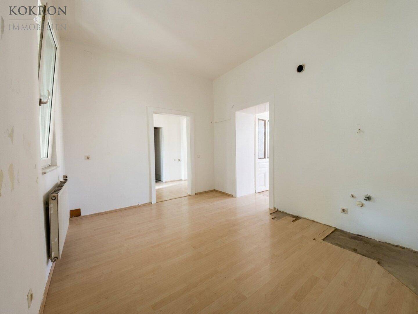 Leerer Raum mit Holzboden und Spuren von Installationen, der auf eine Renovierung wartet.