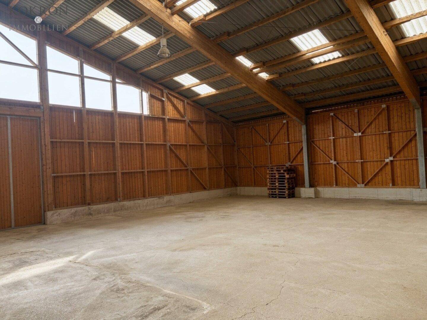 Geräumige Holzhalle mit hohen Decken, sichtbaren Balken und Oberlichtern für viel Tageslicht.