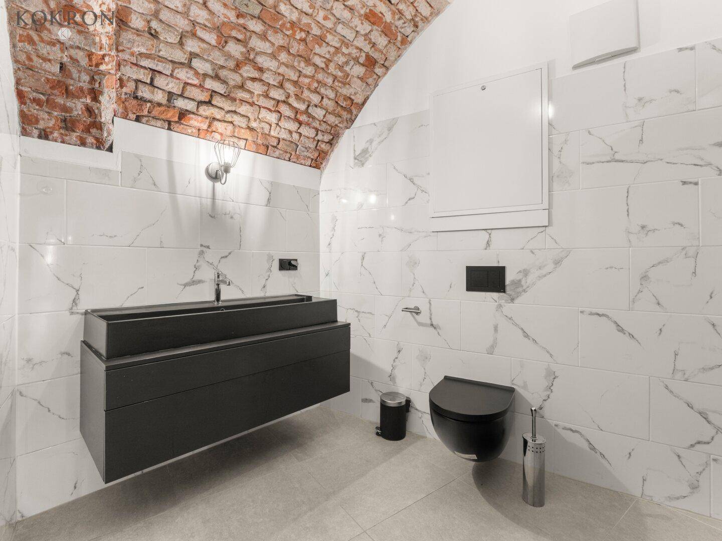 Modernes Badezimmer mit Marmor-Effekt-Fliesen, freiliegendem Ziegelgewölbe und schwebendem Waschtisch in dunklem Design.