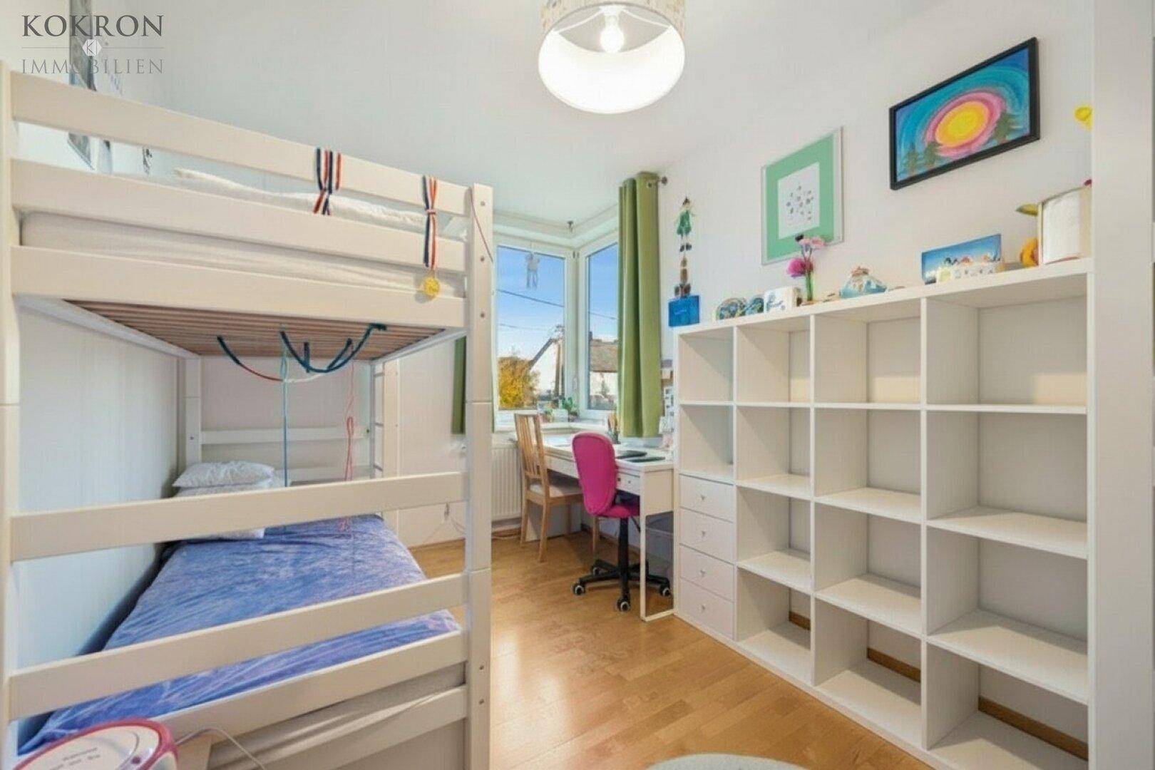 Kinderzimmer mit Etagenbett, Schreibtisch am Fenster und praktischem Regal für Spielzeug und Bücher.
