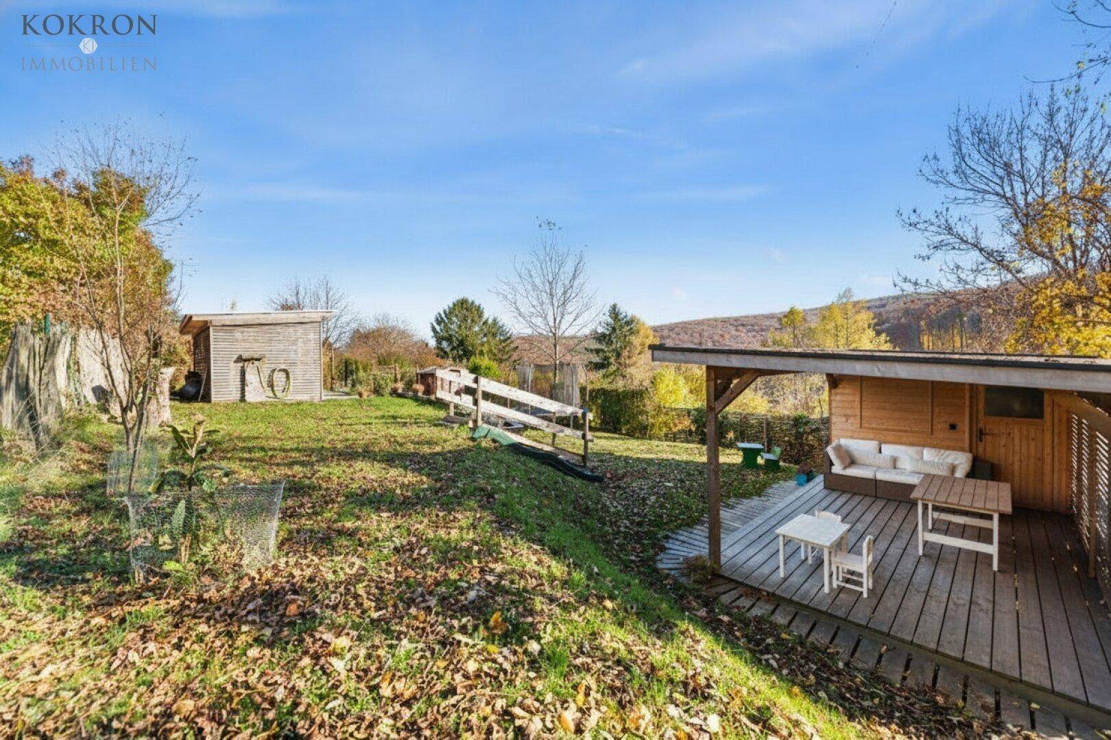 Großer Garten mit Holzterrasse, überdachtem Sitzbereich und Gartenhaus in ländlicher Umgebung.