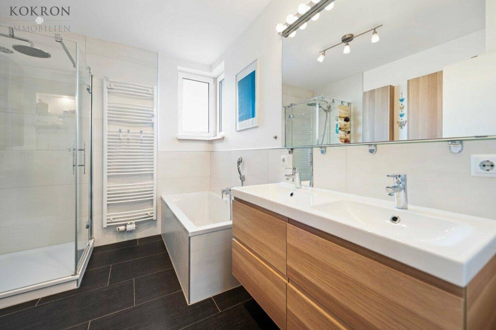 Modernes Badezimmer mit dunklen Fliesen, großer Dusche, Badewanne und Doppelwaschbecken.