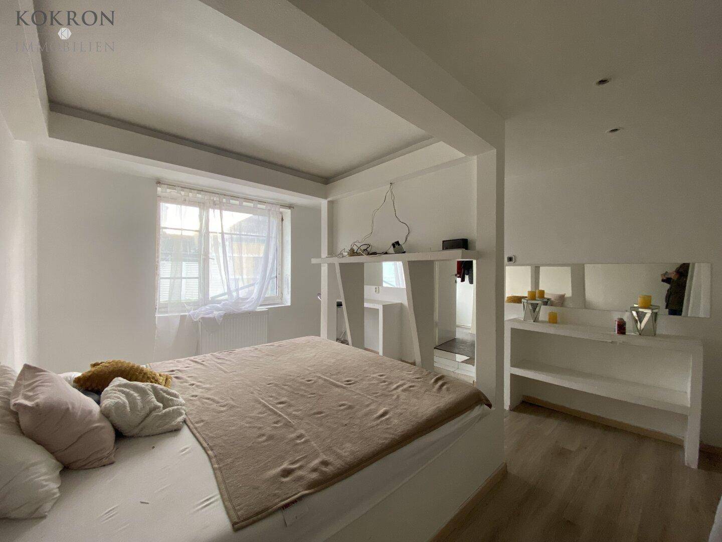 Helles Schlafzimmer mit großem Fenster, Laminatboden und integrierten Ablageflächen.