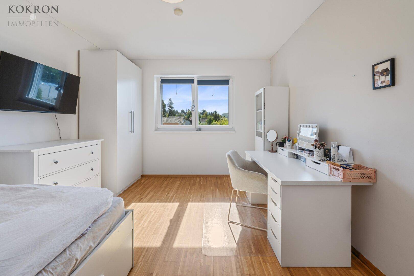Schlafzimmer mit hellem Parkettboden, weißem Kleiderschrank und Schreibtisch, bietet einen ruhigen Rückzugsort.