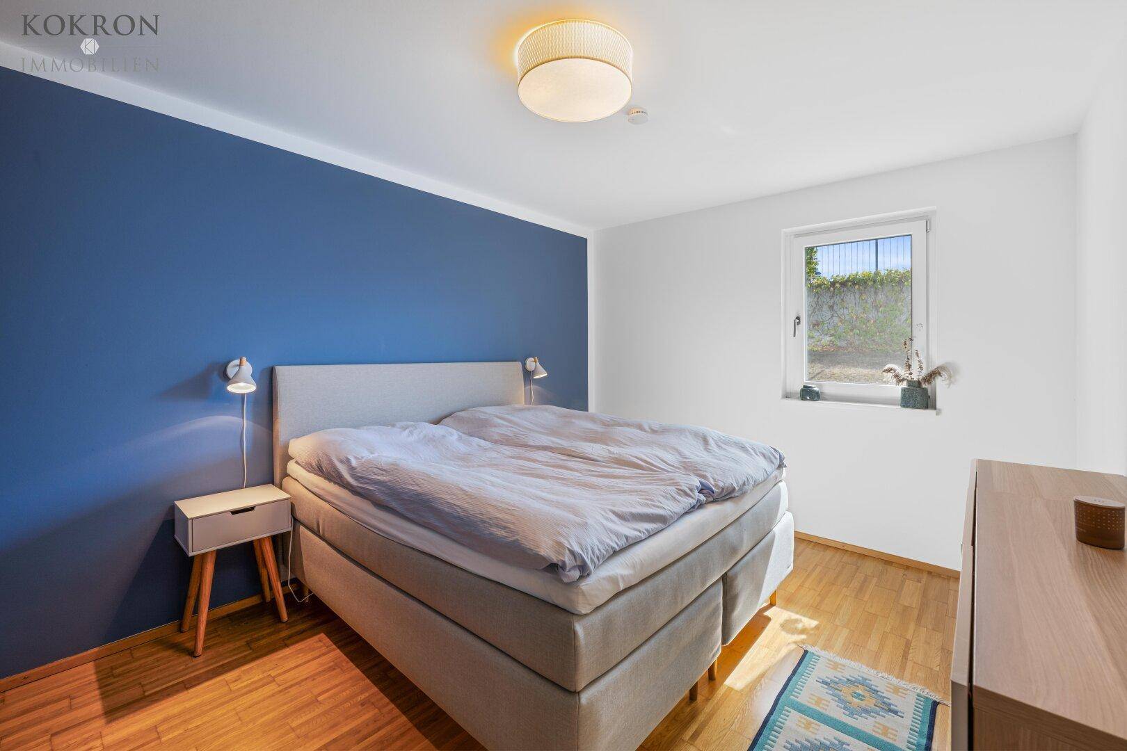 Gemütliches Schlafzimmer mit blauer Akzentwand, Doppelbett und Parkettboden, schafft eine entspannende Atmosphäre.