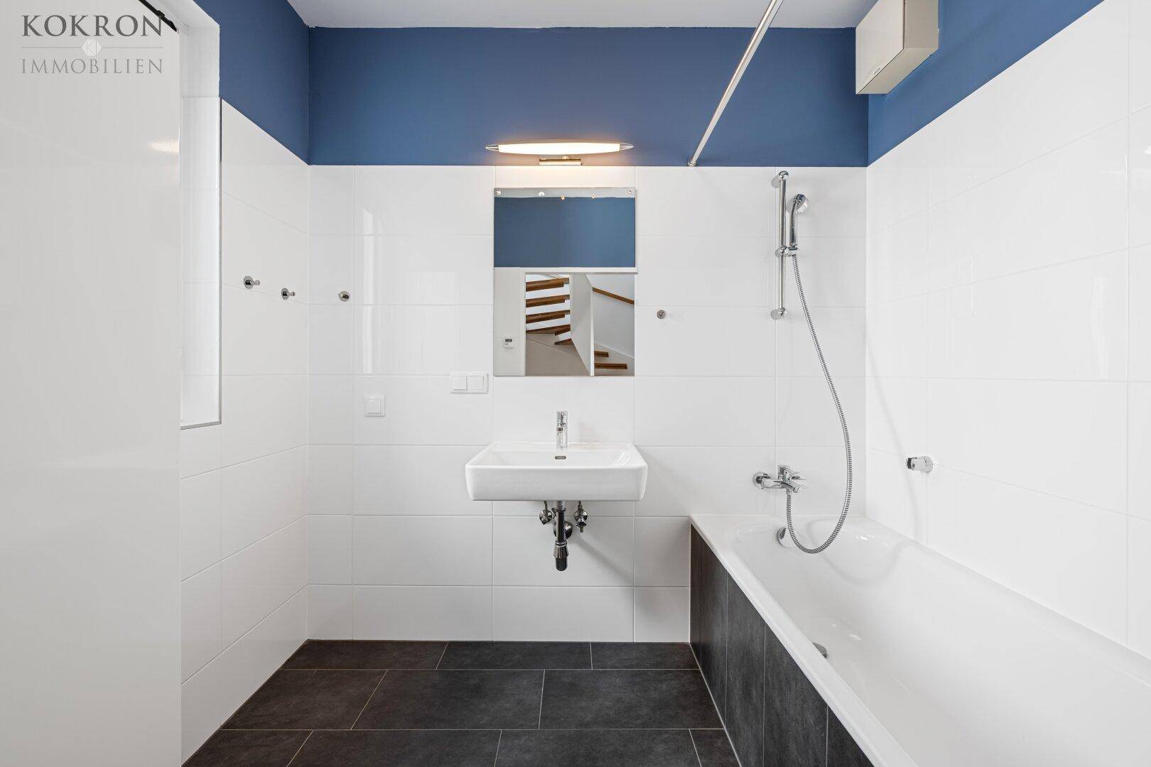 Helles Badezimmer mit Badewanne, Waschbecken und blauer Akzentwand, bietet Komfort und Funktionalität.