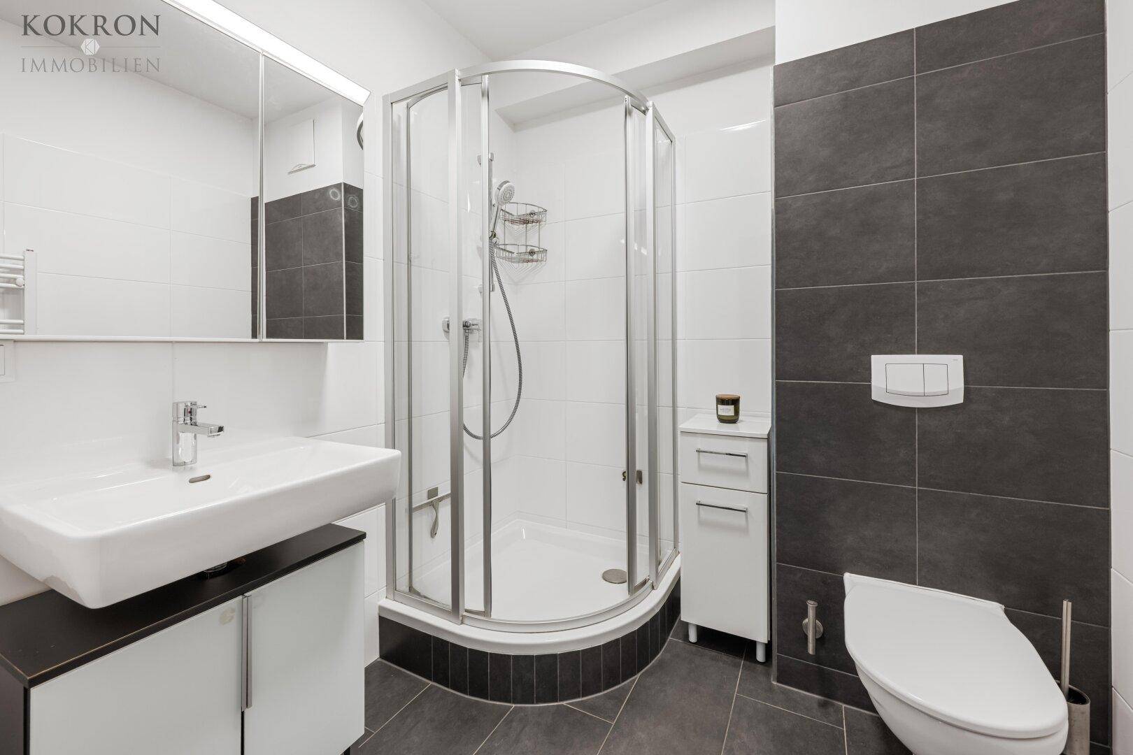 Modernes Badezimmer mit dunklen Fliesen, Duschkabine und wandhängendem WC, funktional und stilvoll gestaltet.