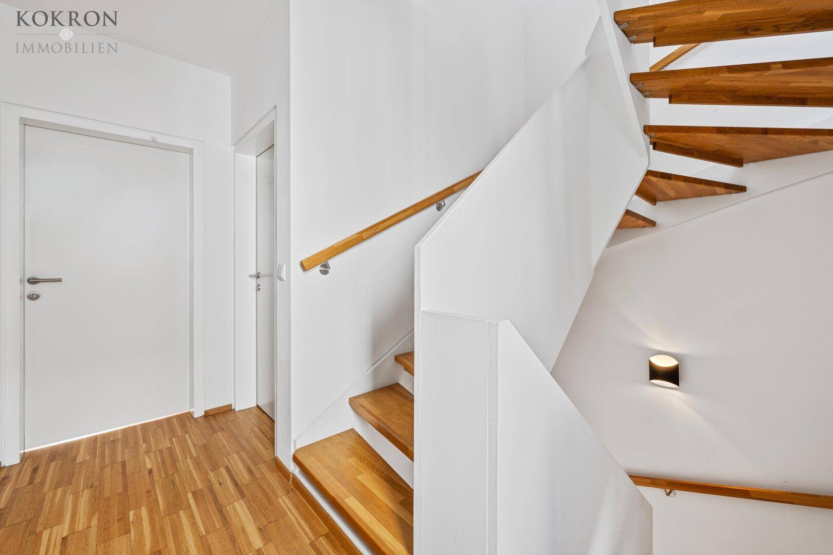 Heller Flur mit Holztreppe und weiß gestrichenen Wänden, der die verschiedenen Ebenen des Hauses verbindet.