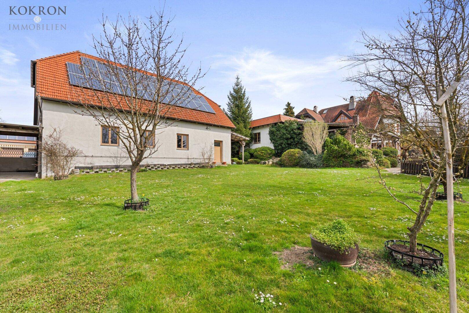 Großzügiger Gartenbereich mit Rasenfläche und Bäumen, im Hintergrund ein Haus mit Solaranlage.
