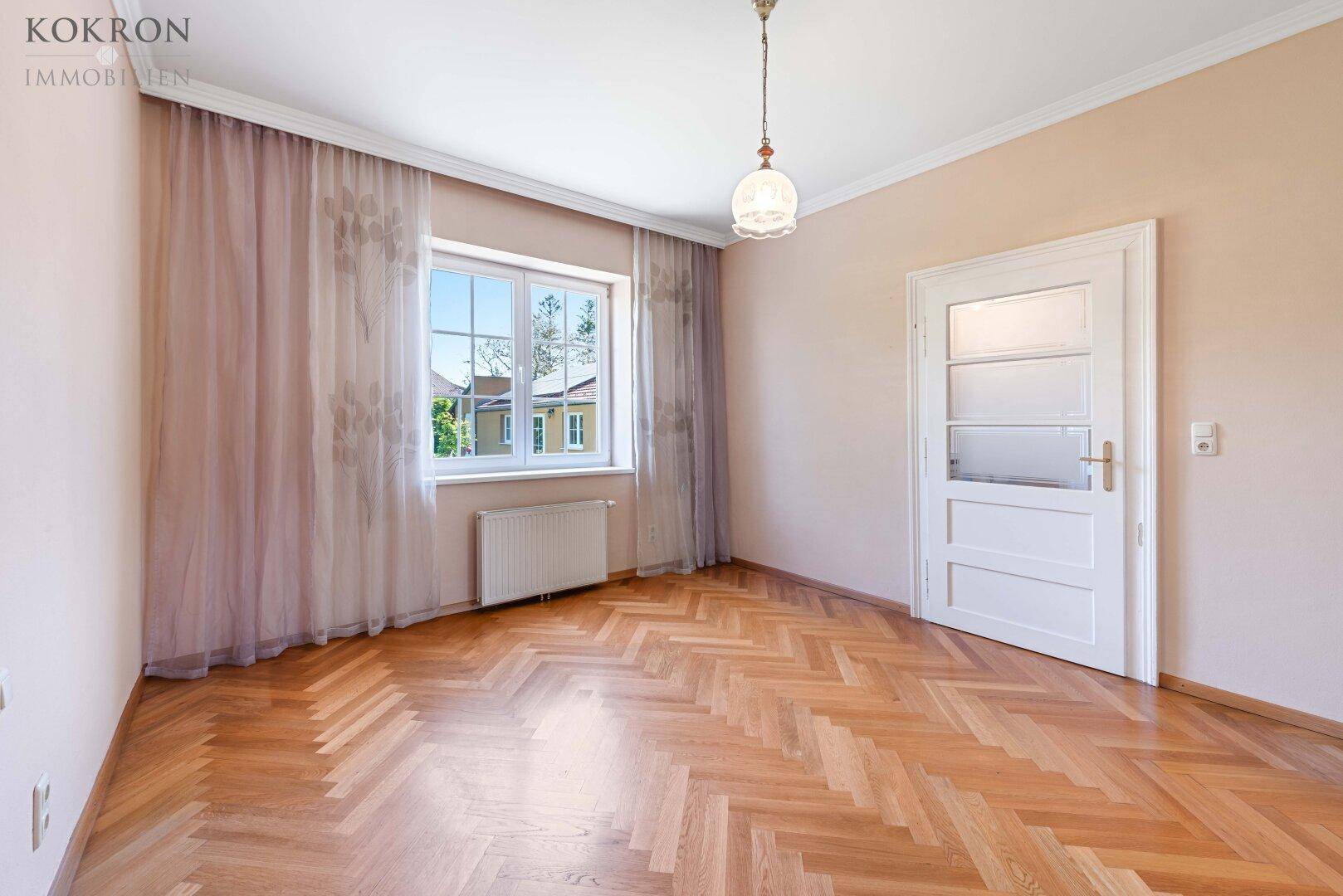 Helles Zimmer mit klassischem Fischgrätparkett und einem großen Fenster, ideal als Schlaf- oder Arbeitszimmer.